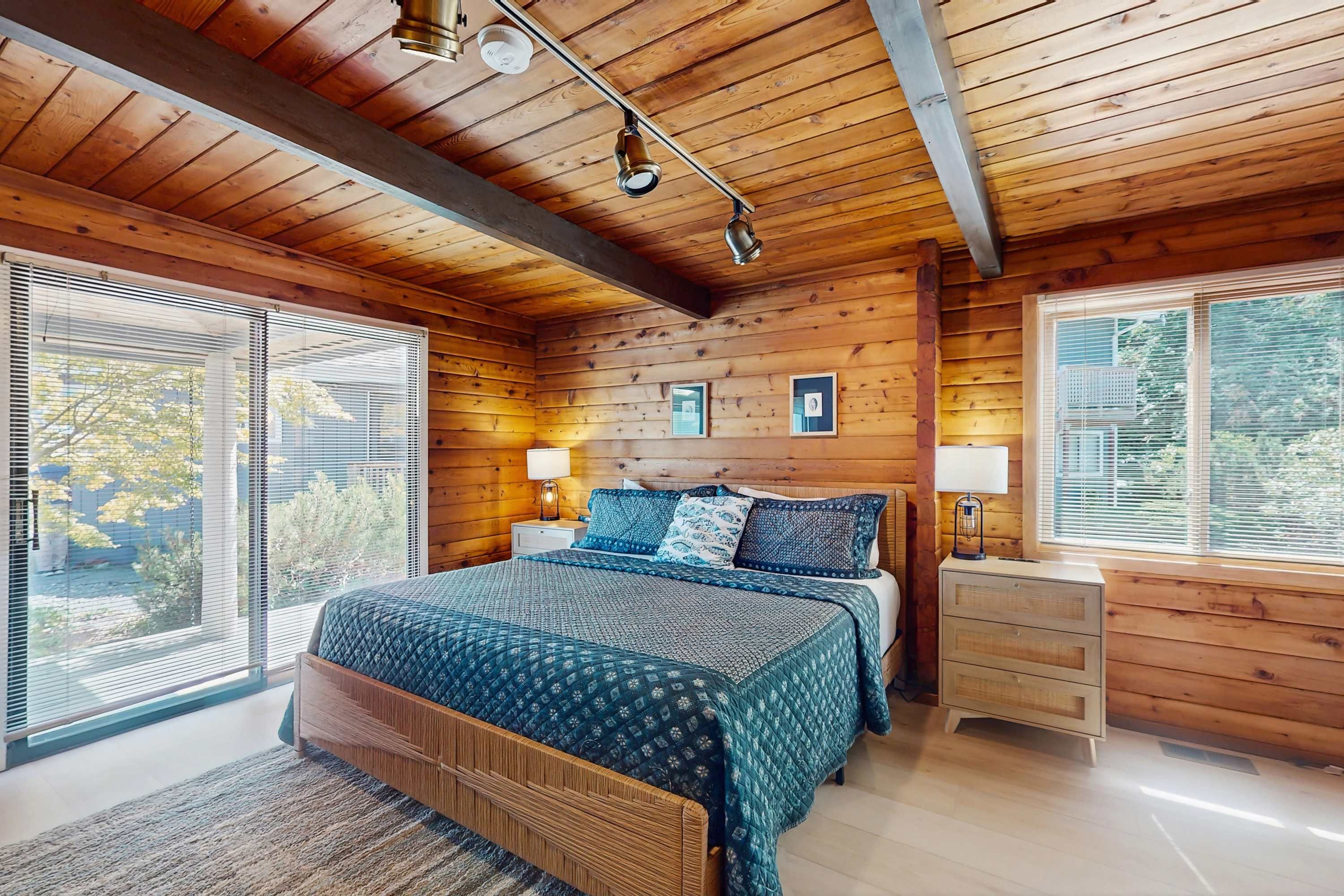 A wooden cabin bedroom with a bed, bedside tables, and a view through the windows.