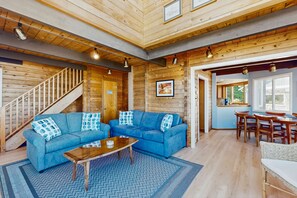 A log cabin interior with a blue sofa set, a wooden coffee table, a staircase, and a dining area with wooden chairs and a table. - Stunning Waterfront Home with Beach Access & Whale Watching (Langley)