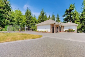 A single-story building with a covered entrance, surrounded by a gravel driveway and a fenced area. - Pet Friendly Waterfront House in Oak Harbor with Sauna and Tennis Court (Oak Harbor)
