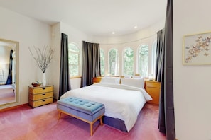 A bedroom with a large bed, a bedside table, a mirror, a window with curtains, and a wall-mounted artwork. - Pet Friendly Waterfront House in Oak Harbor with Sauna and Tennis Court (Oak Harbor)