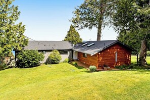 Ein zweistöckiges Haus mit einem geneigten Dach, einem angebauten Holzhaus und einem gepflegten Rasen.