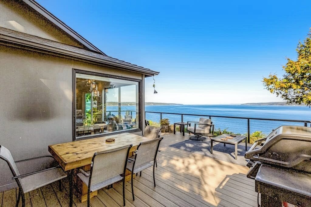 Une terrasse avec coin salon extérieur, un barbecue et vue sur l’eau.