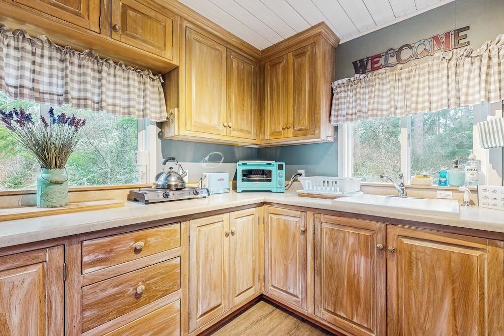 Una cocina con armarios de madera, un tostador, un hervidor y una ventana con un letrero que dice 'WELCOME'.