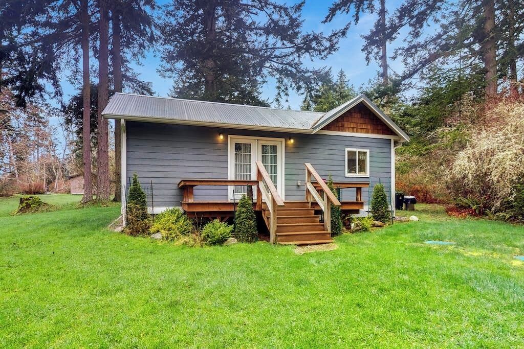 Een gelijkvloers huis met een veranda, houten trap en een kleine voortuin.