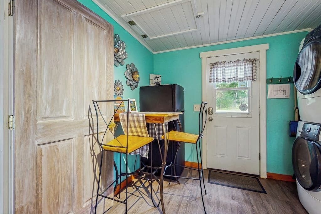 Une pièce de taille modeste équipée d’un lave-linge, d’une petite table avec des chaises, d’un téléviseur et d’une porte avec une fenêtre.