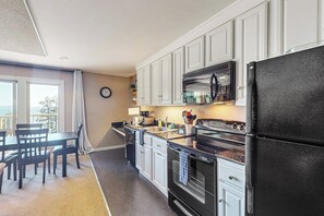 A modern kitchen with white cabinets, a black refrigerator, and a dining area with a table and chairs. - Wonderful Waterfront Escape with Three Balconies and Gas Fireplace (Eastsound)