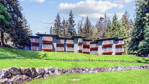 A multi-story hotel with balconies, situated on a grassy slope with trees in the background. - Wonderful Waterfront Escape with Three Balconies and Gas Fireplace (Eastsound)