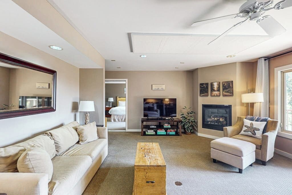 A living room with a sofa, armchair, coffee table, TV, fireplace, and ceiling fan.