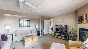 A living room with a sofa, a television, a fireplace, and a ceiling fan.
