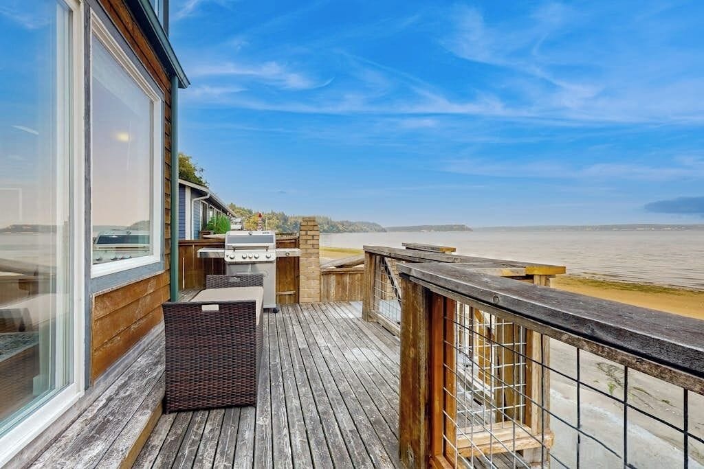 A wooden deck with a grill and seating area overlooking a body of water.