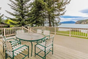 Une terrasse en bois avec une table ronde et des chaises, d’où l’on peut admirer un plan d’eau et des montagnes.
