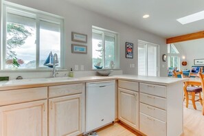 A kitchen with a dishwasher, a sink, and a dining area with chairs and a table. - Stunning Waterfront Home on Lopez Island with Seasonal Hot Tub (Lopez Island)
