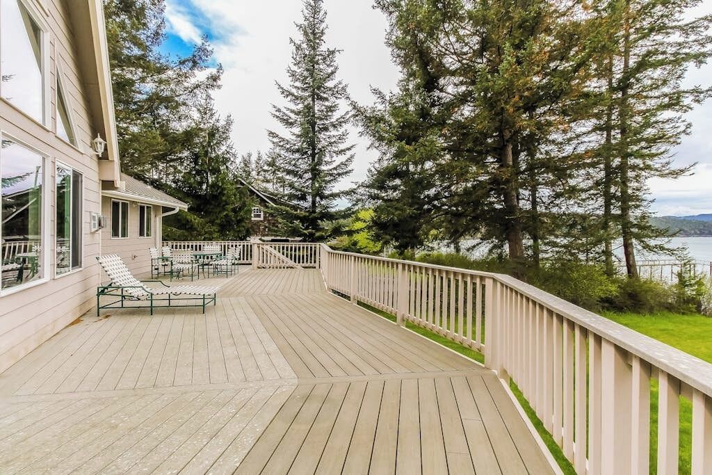 A wooden deck with outdoor furniture, overlooking a body of water and surrounded by trees.
