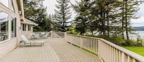 A wooden deck with outdoor furniture, overlooking a body of water and surrounded by trees.