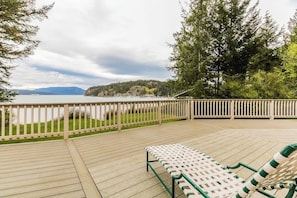 A wooden deck with a view of a lake and hills, and two lounge chairs. - Stunning Waterfront Home on Lopez Island with Seasonal Hot Tub (Lopez Island)