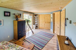 A room with a wooden ceiling, a bed with a colorful bedspread, a wooden dresser, a striped rug, and a wooden door. - Private Waterfront Retreat with Ocean Views and Sauna on Lopez Island (Lopez Island)