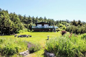 A lodge with a deck, surrounded by a well-maintained garden and dense forest. - Private Waterfront Retreat with Ocean Views and Sauna on Lopez Island (Lopez Island)