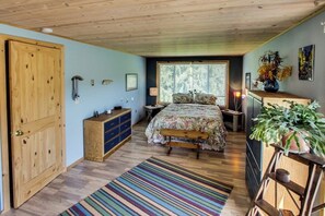 Ein Schlafzimmer mit einem hölzernen Bett, einem Schminktisch, einem Nachttisch, einem Fenster mit Jalousien und einem farbenfrohen Streifen Teppich.