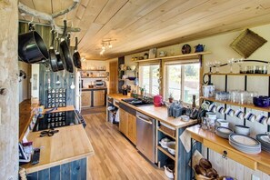 A kitchen with wooden cabinets, a central island, hanging pots, and a window providing natural light. - Private Waterfront Retreat with Ocean Views and Sauna on Lopez Island (Lopez Island)