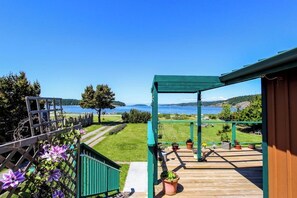 Um deck de madeira com vista para um lago e colinas, uma pérgula verde e plantas em vasos.