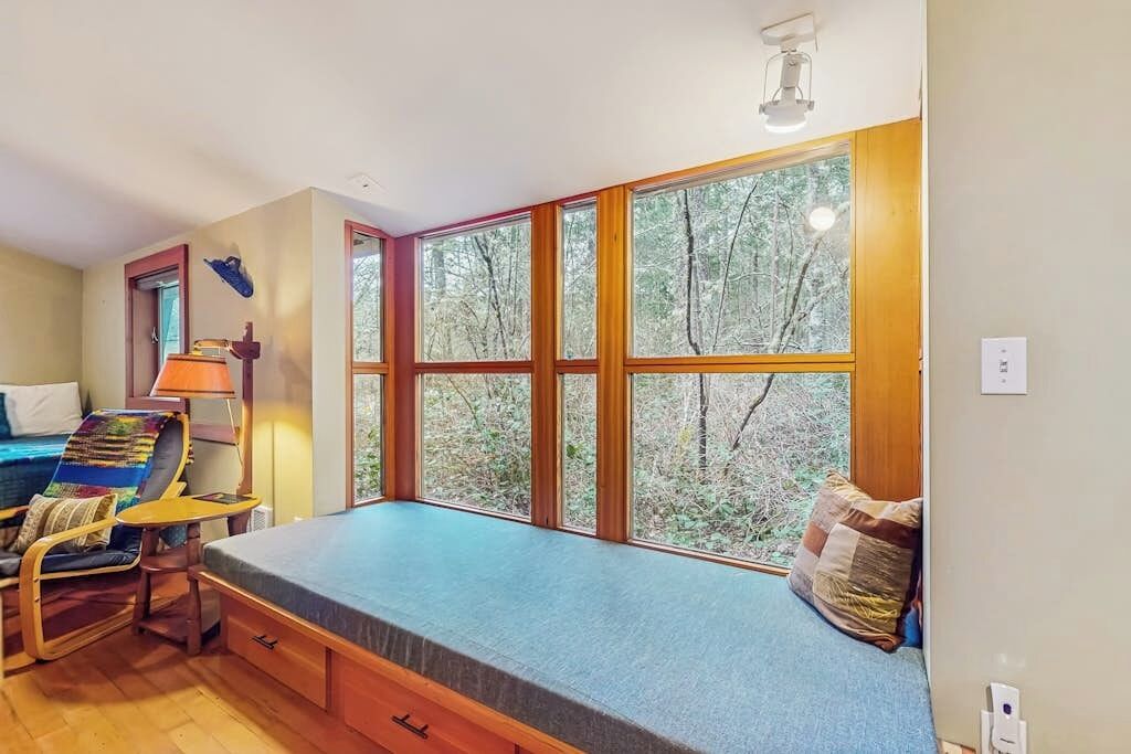 A room with a bed, a chair, a table, and a window with a view of trees.