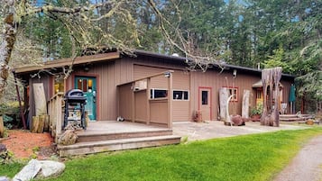 A rustic cabin with a porch, a grill, and a small deck.