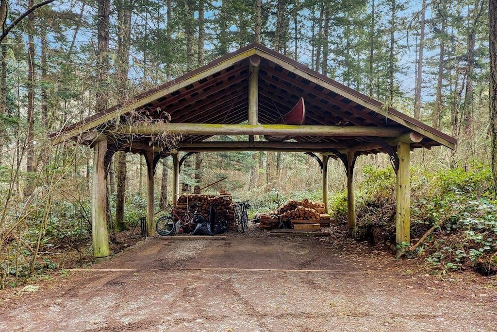 A rustic wooden pavilion with a pitched roof, surrounded by a forested area.