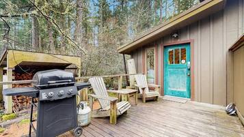Eine Holzterrasse mit Grill, Stühlen und einer Hütte mit einer türkisblauen Tür.