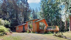 Eine Holzhütte mit Veranda und Kiesweg, umgeben von Bäumen.