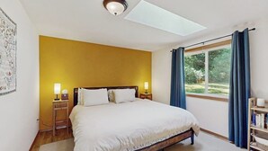Ein Schlafzimmer mit einem Bett, Nachttischlampen, einem Fenster mit Vorhängen, einem Oberlicht und einem Bücherregal.