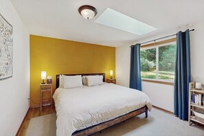 Een slaapkamer met een bed, nachtlampjes, een raam met gordijnen, een dakraam en een boekenplank.