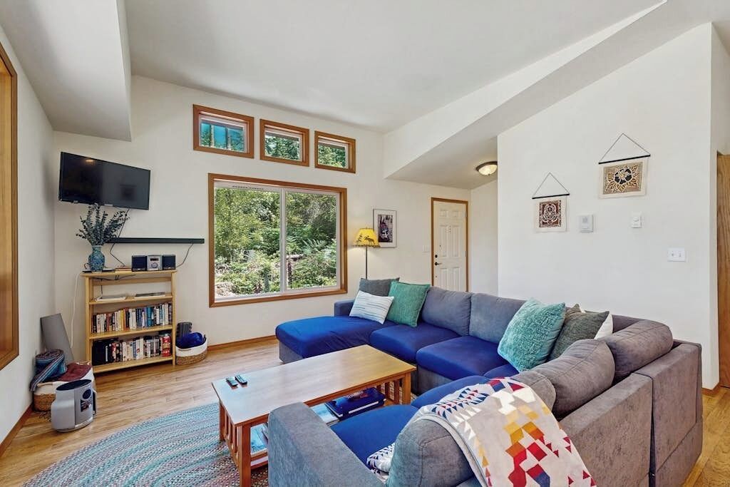 Una sala de estar con un sofá modular, una mesa de centro, una estantería, un televisor de pantalla plana y un ventanal con vistas a zonas verdes.