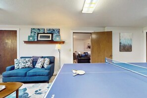 A living room with a blue sofa, a ping pong table, and a framed 'FAMILY' sign on the wall.