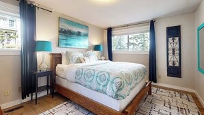 A bedroom with a bed, bedside lamps, a painting, and a window with curtains. - Spacious Dog Friendly 5 Bedroom Beachfront Home with Fenced Yard (Freeland)