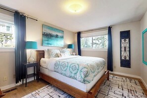 Een slaapkamer met een bed, nachtlampen, een schilderij en een raam met gordijnen.