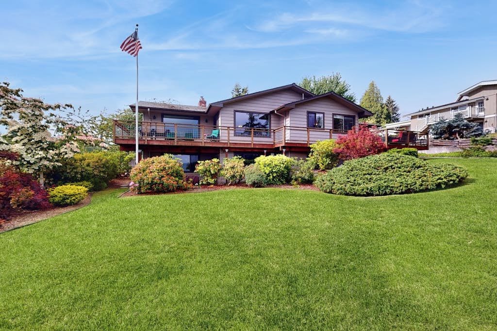 Una casa a due piani con un balcone, circondata da un paesaggio curato e una bandiera americana.