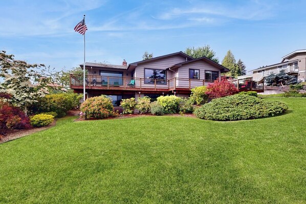 A two-story house with a balcony, surrounded by well-maintained landscaping and an American flag.