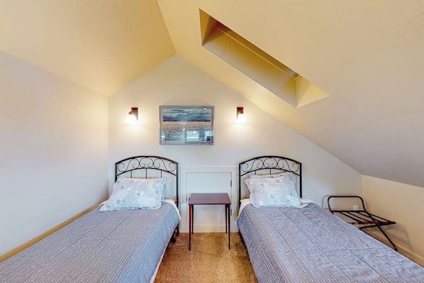 A small, single-room accommodation with two single beds, a small table, and a slanted ceiling.