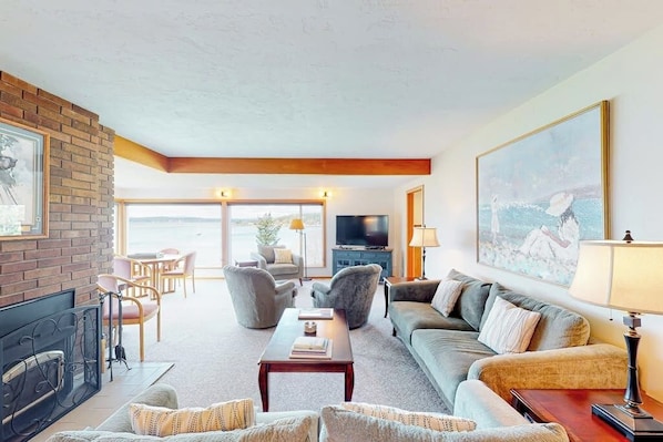 A living room with a fireplace, sofa, and television. There is a large window with a view.