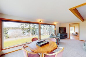 A spacious room with a large window, a dining table with chairs, a sofa, and a television.