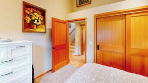 A bedroom with a bed, a dresser, a painting, and a staircase leading to another room. - Stunning Waterfront Home on Fisherman Bay with Sunset Views and Ping Pong (Lopez Island)