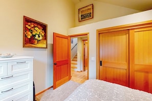 A bedroom with a bed, a dresser, a painting, and a staircase leading to another room.
