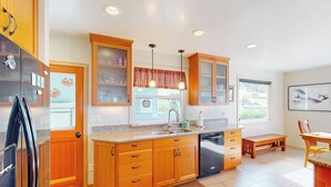 A kitchen with wooden cabinets, a black refrigerator, a sink, and a window with a view. - Stunning Waterfront Home on Fisherman Bay with Sunset Views and Ping Pong (Lopez Island)