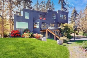Une maison moderne à deux étages, dotée d’une terrasse en bois, d’un escalier et d’un jardin bien entretenu.