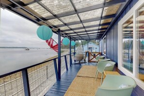 A covered outdoor seating area with a view of the beach, a swing chair, and a table with chairs.