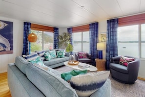 A living room with a sofa, armchairs, a coffee table, and a view of a body of water through large windows. - Stunning Soundfront Home in Coupeville with Private Beach Access and Fire Pit (Coupeville)