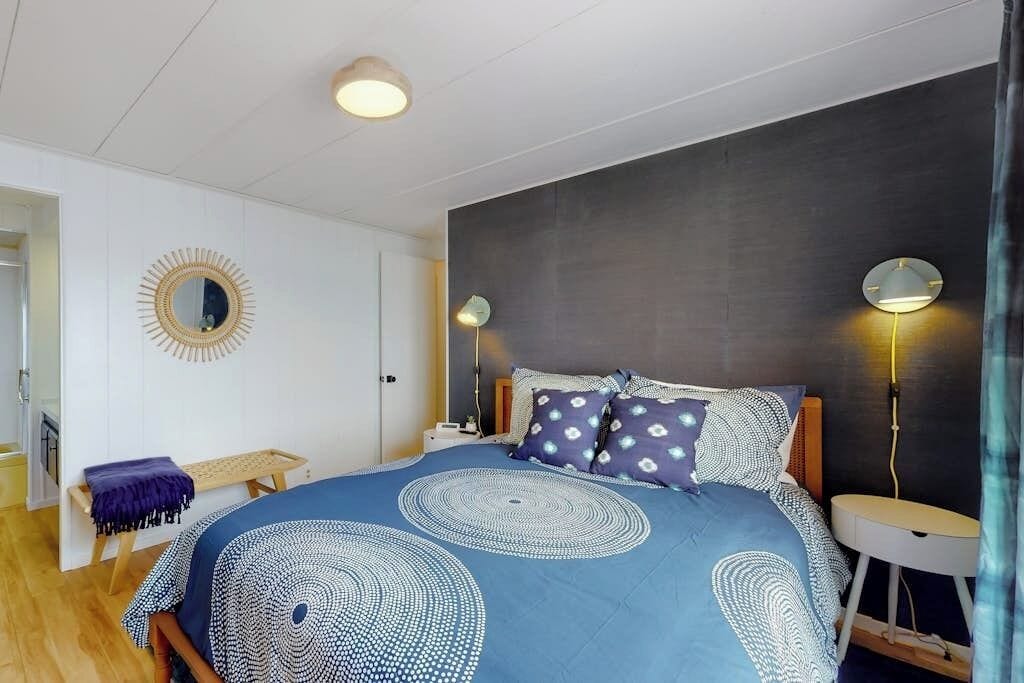 Ein Schlafzimmer mit einem Bett, Nachttischlampen, einer Bank und einem Spiegel an der Wand.