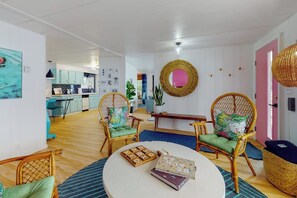 A room with wicker chairs, a round table, and a kitchen in the background.