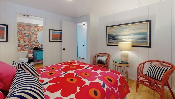 Quarto de hotel com cama, cadeira, mesa com abajur e um quadro na parede.