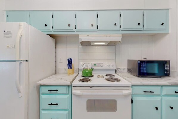 A kitchen with teal cabinets, a white refrigerator, a stove with a kettle, and a microwave.